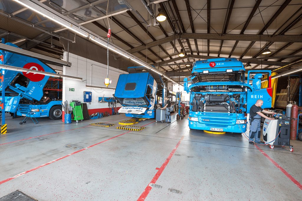 Rein Spedition _ Werkstatt_mehrere Fahrzeuge der Rein Spedition Saarland in der Werkstatt mit einem Mitarbeiter, der ein Gerät bedient